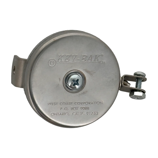 The Key-Bak #481LS-HD Mountable Retractable Reel, featuring a round, silver design with the brand name "KEY-BAK" and manufacturer details engraved on the front, includes a steel cable and comes with an L bracket and hex nut yoke. This heavy-duty key reel is ideal for industrial applications.