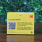 KODAK 653750 Photo ID Color Ribbon for KODAK ID100S and ID200S card printers (YMCKO, 100 prints) in a yellow box with QR code and bilingual instructions for loading the ribbon and cleaning roller, displayed on a wooden surface with a blurred green leafy background. Photographed and sold by Specialist ID, an authorized Magicard dealer.