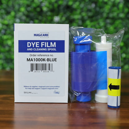 Magicard MA1000K-Blue ribbon cartridge with cleaning spool and cleaning solution in retail packaging on wood surface with green foliage background. Photographed and sold by Specialist ID, an authorized Magicard dealer.