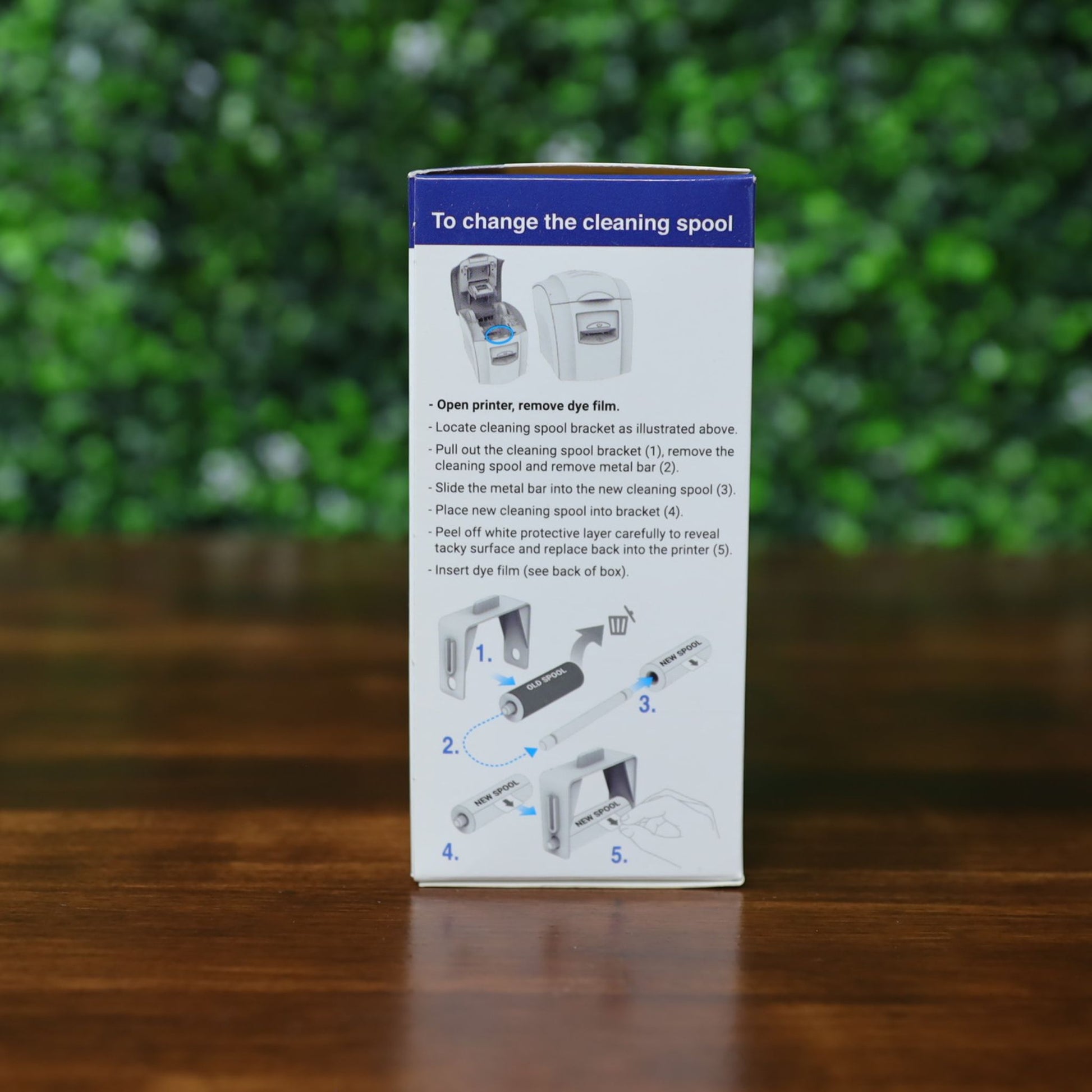 Box with illustrated step-by-step instructions for replacing the Magicard MA1000K GOLD Gold Ribbon – 1000 Prints in a printer, shown against a blurred green background. Photographed and sold by Specialist ID, an authorized Magicard dealer.