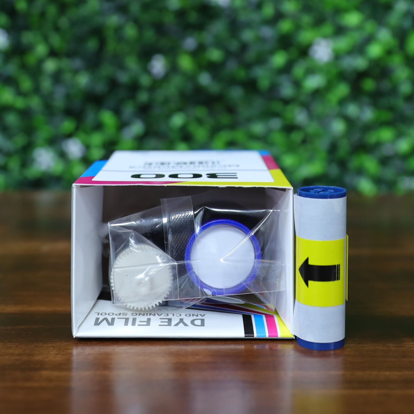 Top-down view of Magicard MC200YMCKO/2 ribbon kit showing interior packaging with ribbon spool, cleaning roller, and plastic wrap inside the branded box. Includes separate cleaning roller placed upright for display. Photographed and sold by Specialist ID, an authorized Magicard dealer.