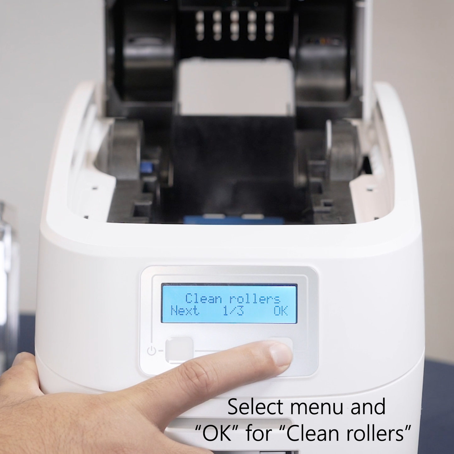 ID badge machine with digital display and hand selecting 'Clean rollers' option.