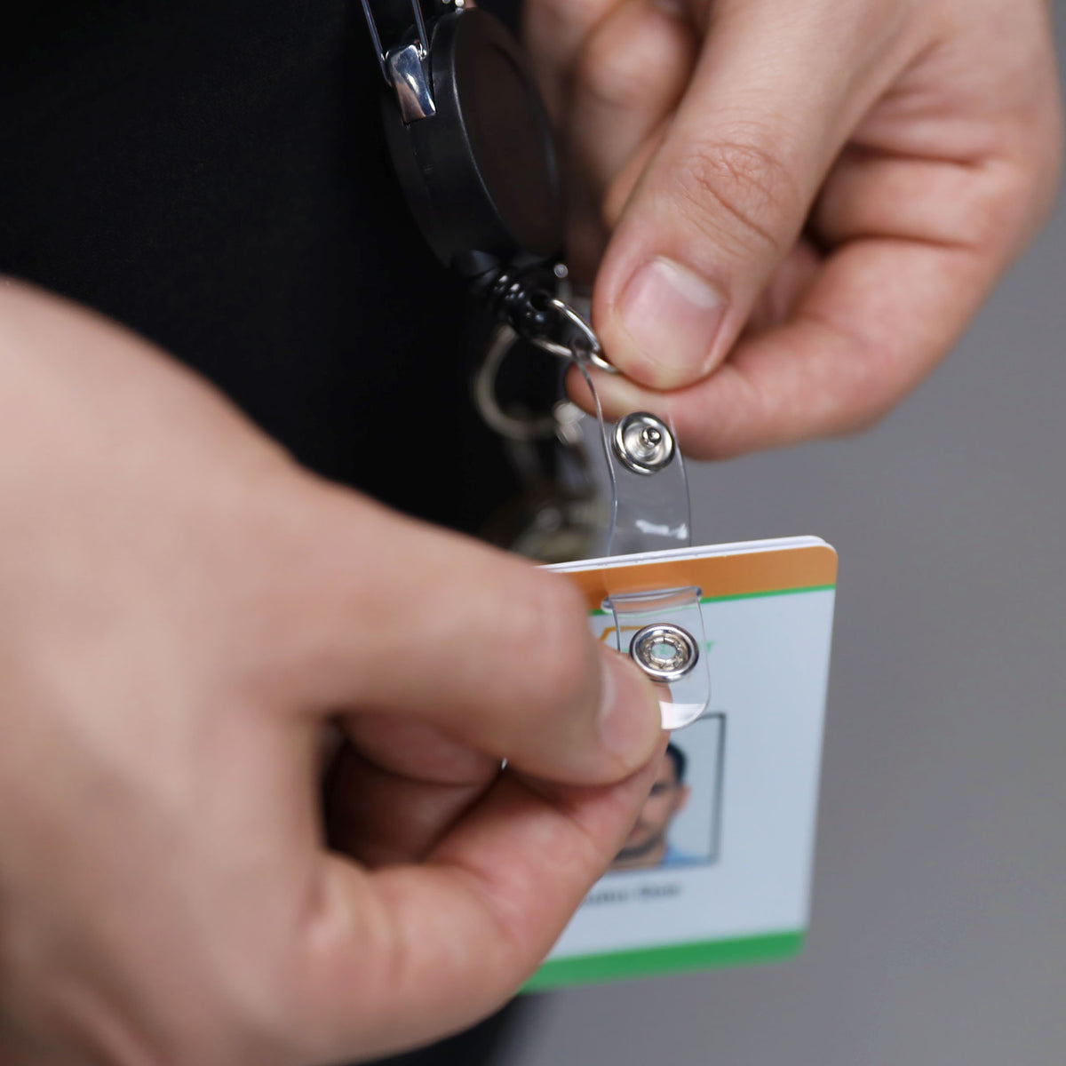 Hands threading the vinyl ID strap through the slot of a dual ID badge holder