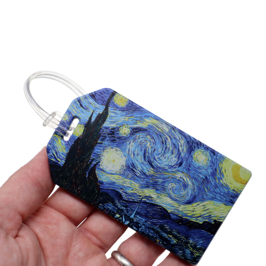 A hand holds a rectangle-shaped luggage tag resembling the Van Gogh-inspired "Starry Night" design, complete with a clear loop. Sold by Specialist ID.