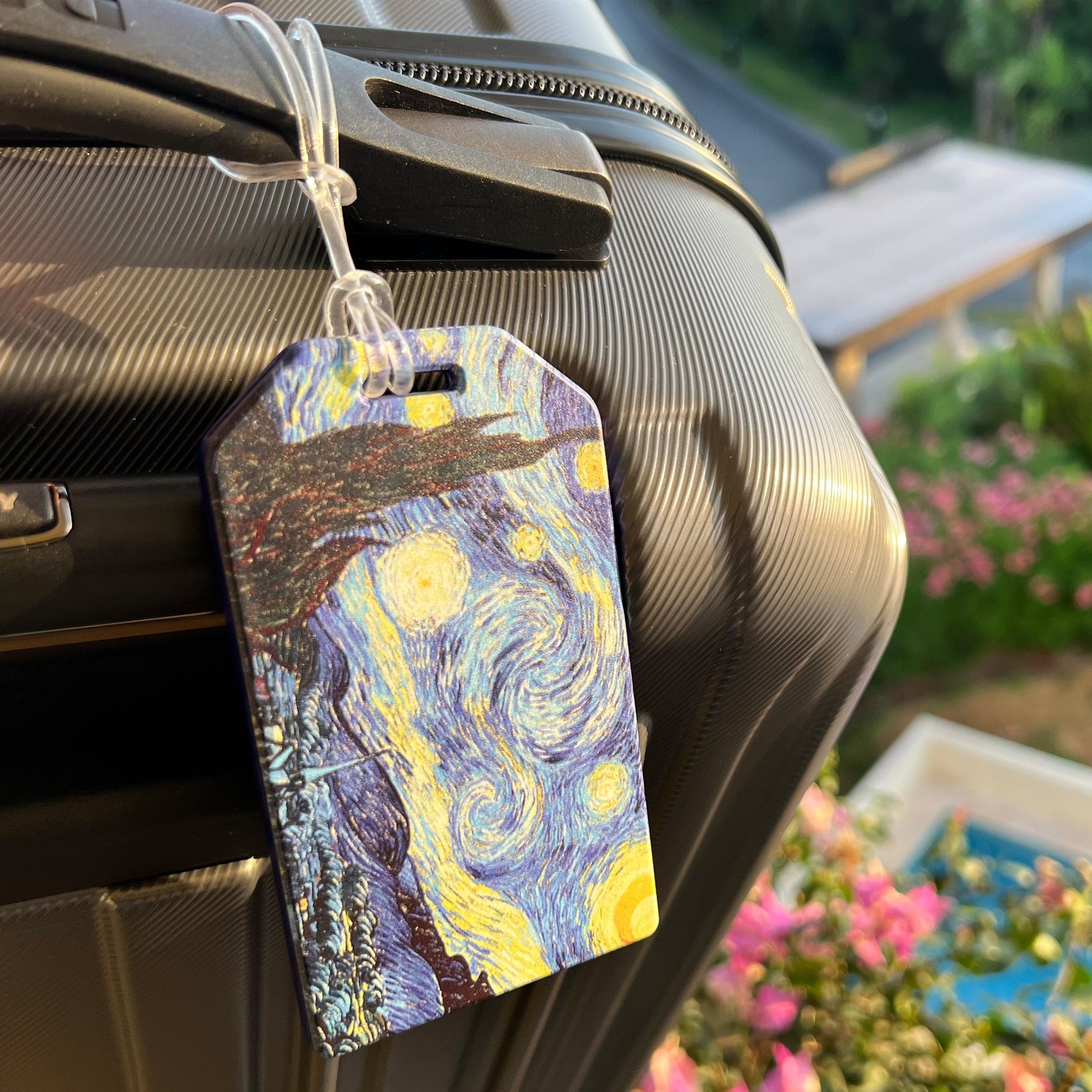 Starry Night luggage tag attached to a suitcase handle outdoors