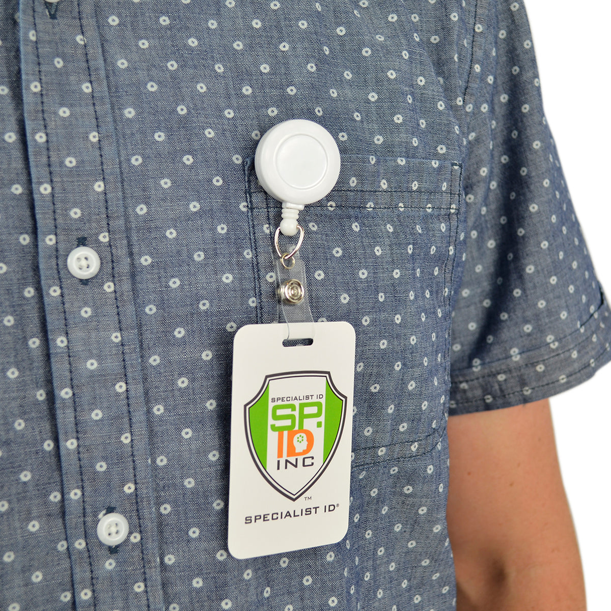 White retractable badge reel clipped to a shirt pocket with ID badge.