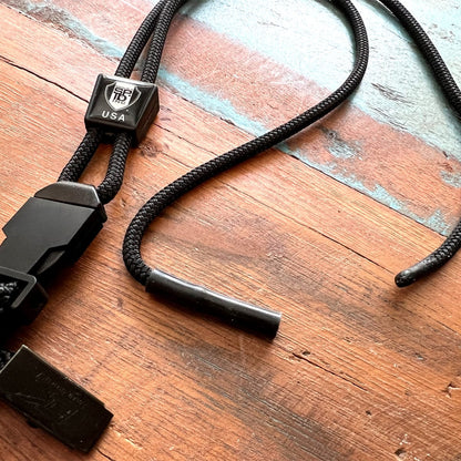 A Black EK Lanyard Plus with Soft End And Fused Clip (10761) by EK USA wrapped in a plastic covering, lying on a wooden surface. Sold by Specialist ID.