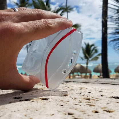 A hand is holding a Heavy Duty Clear Vinyl Horizontal Badge Holder With Resealable Zip Top (1815-1010) on a stone surface, with palm trees and a beach in the background.