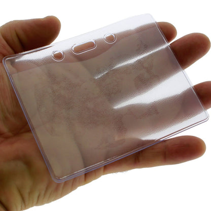A person holds a Clear Vinyl Horizontal Military Card Size Badge Holder (P/N 1815-1200) with two holes for a lanyard, perfect for displaying a government or military card.