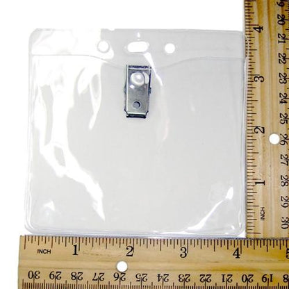 Clear Vinyl Horizontal Badge Holder With Clip And Chain Holes (P/N 1815-1405), lying next to two wooden rulers marked with inch measurements.