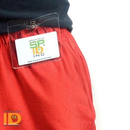 A Clear Vinyl Horizontal Badge Holder With Clip And Chain Holes (P/N 1815-1405) with a Specialist ID badge is clipped to the waistband of red pants using a 2-hole clip & slot.