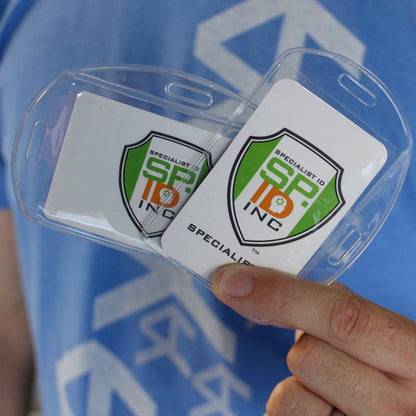 A person holds two Vertical / Horizontal Durable Clear Vinyl ID Badge Holders (1815-1600) with logo cards inside, each attached to transparent vinyl sleeves, perfect for a professional workplace environment.