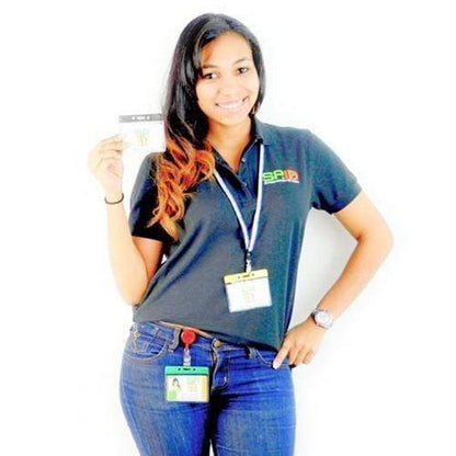 A woman in a dark polo shirt and blue jeans, wearing a lanyard with a Horizontal Vinyl Badge Holder with Color Bar Top - Great for Color Coding Access and ID (1820-100X), is smiling and holding up a card.