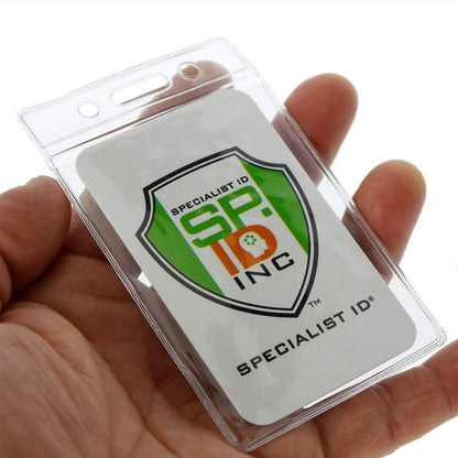 A hand holds a Standard Vertical Vinyl ID Badge Holder (1820-1050) with a credit card-sized ID card inside, displaying the logo "Specialist ID Inc." and a shield emblem with the text "SP ID" on a green and white background.