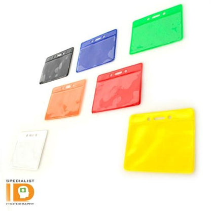 Seven transparent, color-coded Horizontal Vinyl Color-Back Badge Holders (P/N 1820-200X) in black, blue, green, red, orange, yellow, and clear are arranged in a pattern on a white background. "Specialist ID" is branded in the lower left corner. Perfect for quick identification or student bus assignment needs.