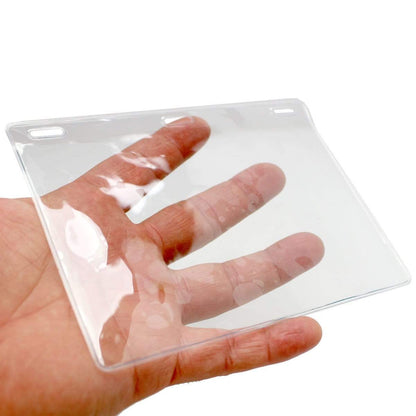 A hand holding a Clear 6X4 Vinyl Horizontal Large Event Badge Holder (1840-1615) with a transparent, rectangular plastic design featuring two slots at the top.