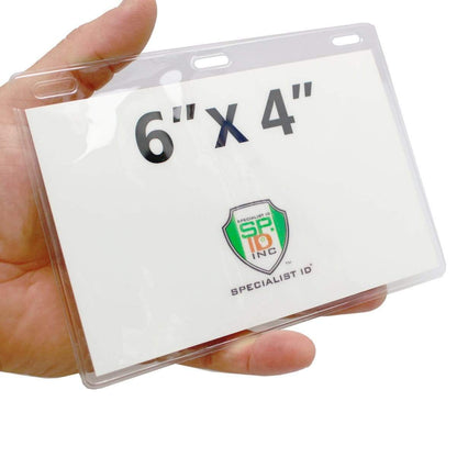 A hand holding an oversized ticket and credential holder containing a card marked "6'' x 4'." The clear plastic double-sided window reveals a logo and text reading "Clear 6X4 Vinyl Horizontal Large Event Badge Holders (1840-1615).