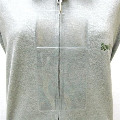 A Clear 4" X 7 1/2" Vinyl Vertical Large Badge Holder With Two Pockets (P/N 1840-5052) hangs around the neck of a person wearing a gray zip-up sweatshirt with green text on it.