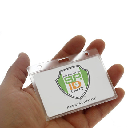 A hand holding a clear plastic badge holder with a "Specialist ID" logo on an insert featuring a shield and "SP INC" text. This Horizontal Rigid Plastic Badge Holder - Frosted Card Dispenser (P/N 1840-6000) offers exceptional ID badge protection, ensuring both durability and security.