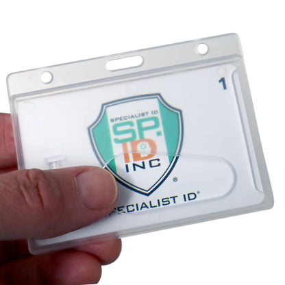 A hand holds a clear plastic holder containing an ID card with the text "SPECIALIST ID" and a green and orange shield logo. The Horizontal Rigid Plastic Badge Holder - Frosted Card Dispenser (P/N 1840-6000) ensures optimal ID badge protection.