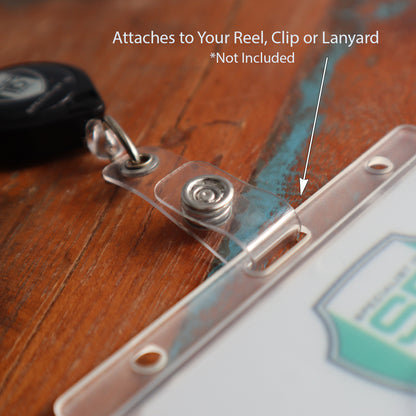 A close-up image of a clear, rigid badge holder with an attached clip on a wooden surface. The text indicates it attaches to a reel, clip, or lanyard for optimal ID badge protection, which are not included. The product is the Horizontal Rigid Plastic Badge Holder - Frosted Card Dispenser (P/N 1840-6000).