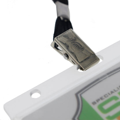 Close-up view of a metal clip attached to a black lanyard, holding a white card with a green and gray design. The card sits securely in a Horizontal Rigid Plastic Badge Holder - Frosted Card Dispenser (P/N 1840-6000), which has two holes at the top edge.