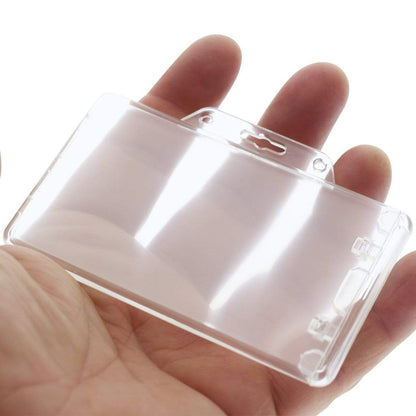 A hand holding a Clear Horizontal Permanent Locking Plastic Card Holder (P/N 1840-6040) with a slot for attaching to a badge reel or lanyard.