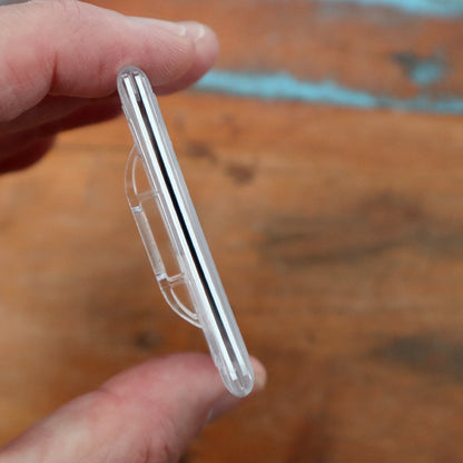 A hand holding a Frosted Vertical Rigid 2-Card Access Card Dispenser (1840-6550) designed to store a single object, possibly a small electronic device or accessory, against a wooden background.
