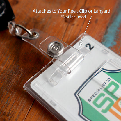 Close-up of a clear plastic vertical badge holder with a clip attachment, labeled "Attaches to Your Reel, Clip or Lanyard." The badge inside displays a logo and a partial view of text. Ideal as an ID badges holder or Frosted Vertical Rigid 2-Card Access Card Dispenser (1840-6550).