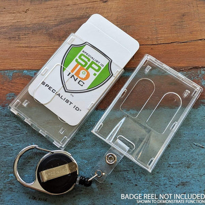 Rigidwear Clear Vertical 2-Card Badge Holder 1840-6560 (Jam P/N 706-NN2) with a green and orange "Specialist ID" insert, key ring, and retractable reel on a wooden surface. Text in the corner reads "Badge reel not included. Shown to demonstrate function.