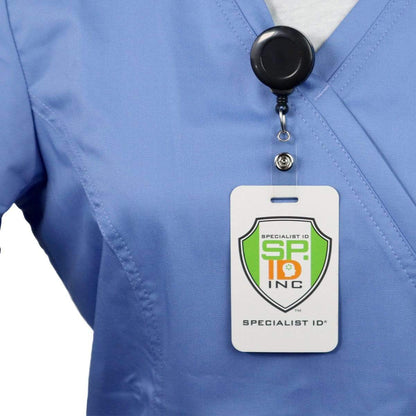 Person wearing a blue scrub top with an ID badge clipped to the chest. The badge, attached via a **"No Twist" Badge Reel With Clear Vinyl Strap And Belt Clip (P/N 2120-305X)**, displays a green and orange shield logo with "Specialist ID Inc" written below it.