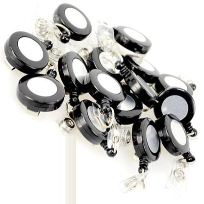 A pile of Black Badge Reel with Silver Metallic Sticker and Belt Clip (2120-3151) with white centers, transparent clips, and a sleek belt clip is complemented by a subtle silver metallic sticker, ensuring both style and functionality.