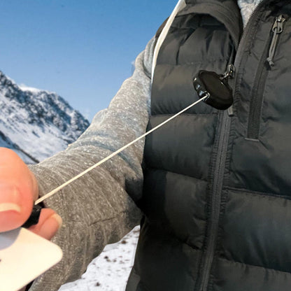 A person wearing a gray jacket is holding a Ski Pass and Sports Retractable Reel (P/N 2120-4001) with the badge extended, standing in front of a snowy mountain backdrop.