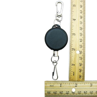 A black Ski Pass Holder Retractable Heavy Duty Sport Reel (P/N 2120-4101) with two metal clips is shown next to a wooden ruler marked in inches.