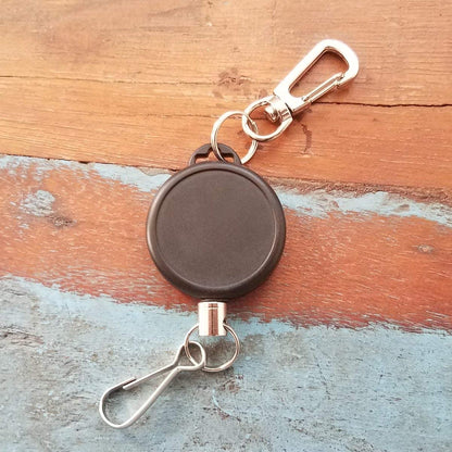 A Ski Pass Holder Retractable Heavy Duty Sport Reel (P/N 2120-4101) is placed on a wooden surface with some blue paint spots, making it perfect for a ski pass holder or retractable sport reel.