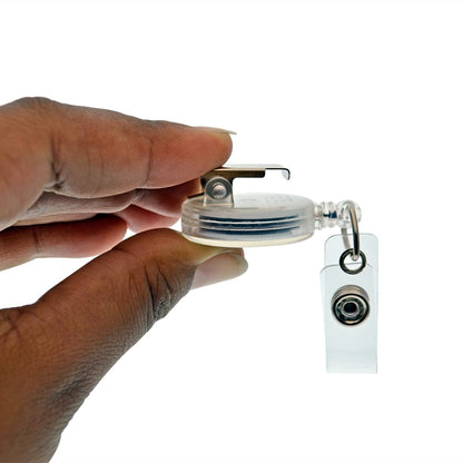 A hand holding a Translucent Retractable Badge Reel with Non-Swivel Spring Clip (P/N 2120-473X), featuring a clip attachment and a retractable cord for easy access. Sold by Specialist ID.