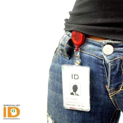 A person wearing blue jeans has a Translucent Retractable Badge Reel with Non-Swivel Spring Clip (P/N 2120-473X) attached to their waistband. The ID card displays a silhouette image and text.