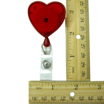 A Heart Shaped Badge Reel With Rotating Spring Clip (P/N 2120-761X) is placed next to a wooden ruler, demonstrating its dimensions.