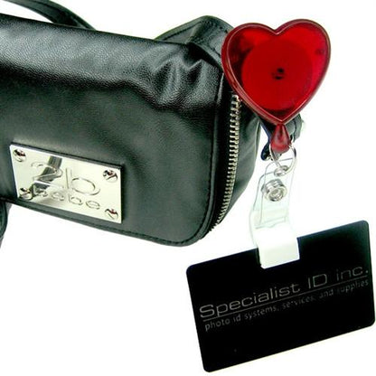 A black ID holder with "Specialist ID Inc." text is attached to a black bag by a Heart Shaped Badge Reel With Rotating Spring Clip (P/N 2120-761X) with a retractable cord.