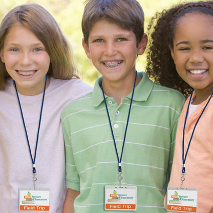 Three children with field trip name badges from Stewart Elementary are smiling outdoors. The child in the center has braces, and the child on the right is wearing a headband and an ID card holder on a Round Breakaway Lanyard with Swivel Hook (2137-200X).