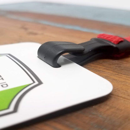 Close-up of an Adjustable Breakaway Lanyard Great For All Sizes (2137-203X) with a wide plastic hook attached to a white card with green and black markings, placed on a wooden surface.