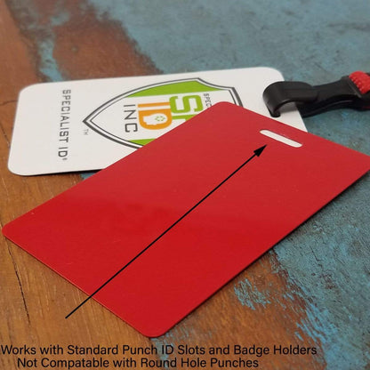 A red ID card with an arrow pointing to the slot punch, placed on a wooden surface beside a white ID card with a brand logo. Text below reads, "Works with Standard Punch ID Slots and Badge Holders. Ideal for use with no twist flat braid and Breakaway Lanyard with No Twist Plastic ID Clip - MRI and Metal Detector Friendly (2137-474X) styles. Not Compatible with Round Hole Punches.
