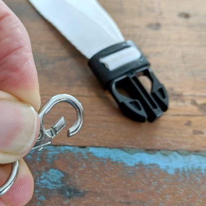 Close-up of a hand holding a Quick Release Clasp in front of a Premium Wide Breakaway Lanyard with Detachable Lobster Claw Clasp - Great for Keys or Badges (2138-362X) with a black plastic clip, resting on a wooden surface.