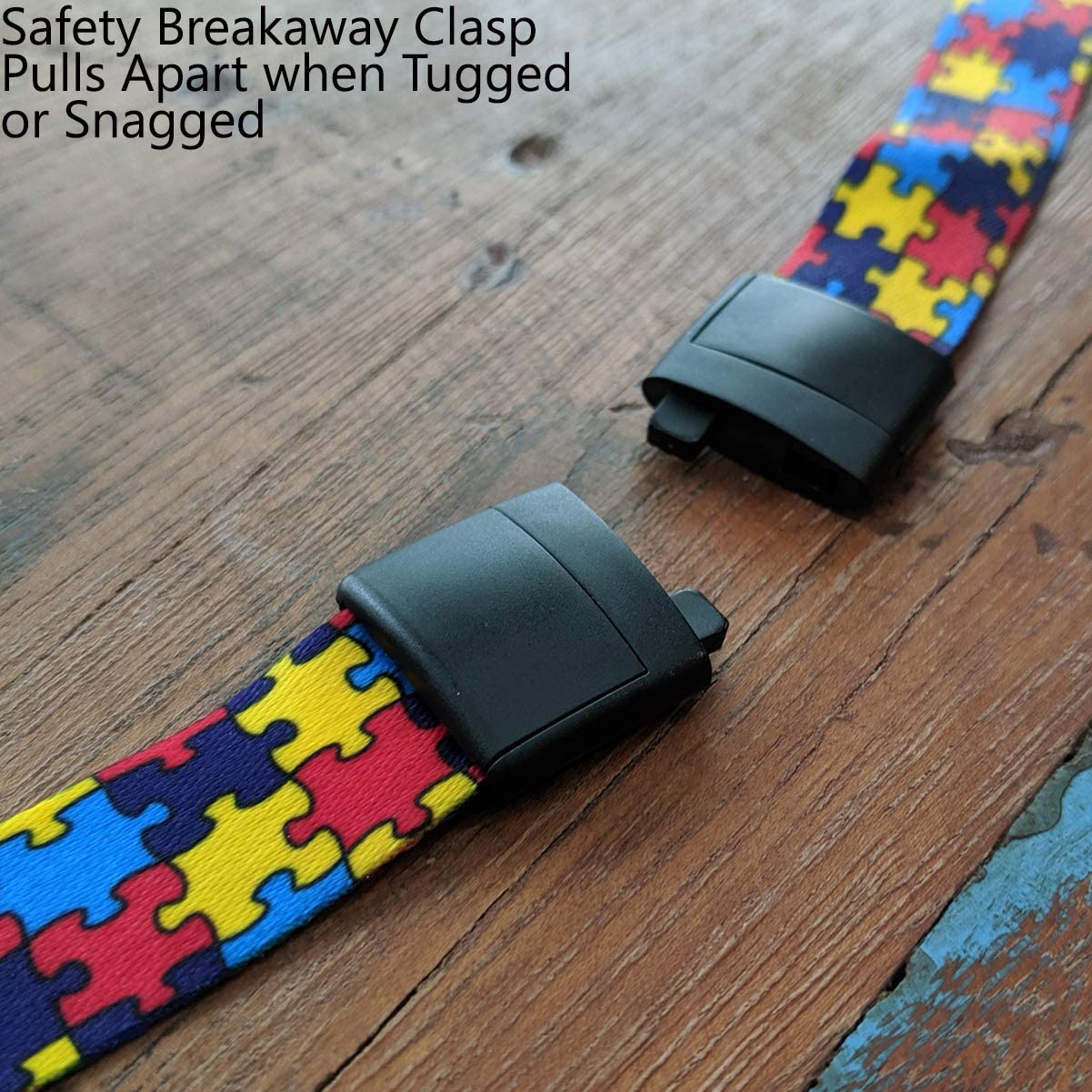 Close-up of a safety breakaway clasp on an Autism Awareness Flat Breakaway Lanyard With Swivel Hook (2138-5281, 2138-5282), showing two detached ends of a colorful puzzle-patterned band on a wooden surface. Text indicates the clasp pulls apart when tugged or snagged.