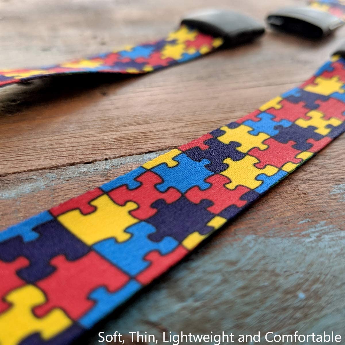 Close-up of a colorful Autism Awareness Flat Breakaway Lanyard With Swivel Hook (2138-5281, 2138-5282) puzzle piece patterned strap on a wooden surface, with text at the bottom that reads, "Soft, Thin, Lightweight and Comfortable.