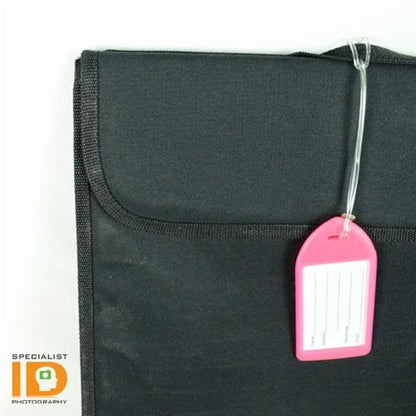A black fabric folder with a pink and white luggage tag attached by 9" Plastic Colored Worm Loop Straps (P/N 2410-210X). The folder has a flap closure, and the words "Specialist ID Photography" appear in the bottom left corner.