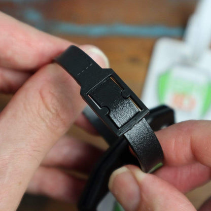 Hands holding a Plastic Luggage Strap with Post and Notch -Textured (2430-201X), showcasing the durable travel strap's clasp mechanism in detail. Blurred objects in the background.