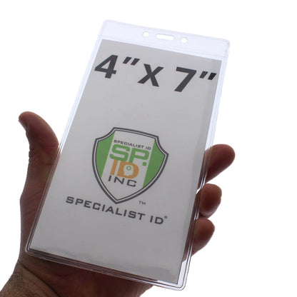 A hand holding a 4 X 7 Clear Vertical Large Event Badge Holder (306-4258) labeled "4" x 7"" with a "Specialist ID Inc" logo inside, perfect for keeping visible credentials secure and hands-free during large events.