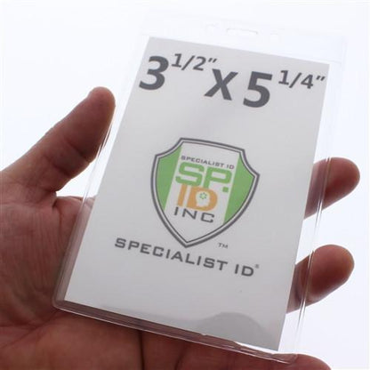 A hand is holding a 3 1/2" X 5 1/4" Clear Vertical Large Event Badge Holder (P/N 306-46), displaying a logo with the text "Specialist ID SP INC".