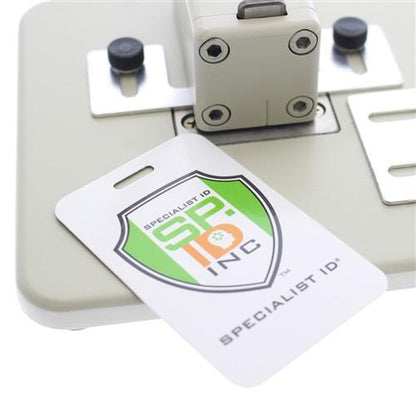 A close-up image of a Specialist ID badge with the company's logo, placed on a Heavy Duty Table Top Slot Punch With Adjustable Guides (P/N SPID-9620) used for punching holes in badges.